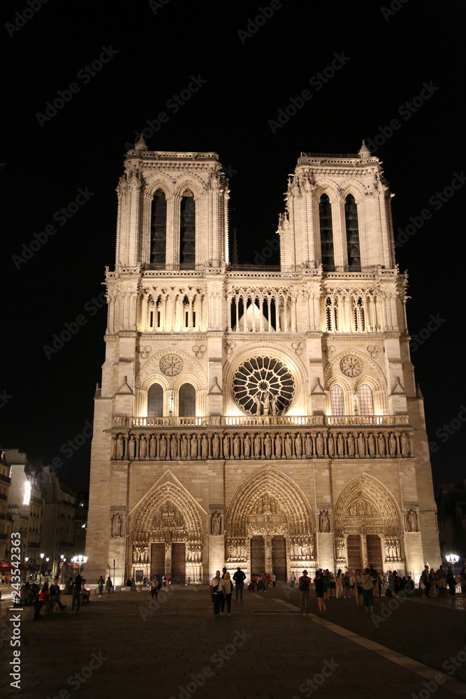 facade of the Notre Dame cathedral in Paris by night with some tourists