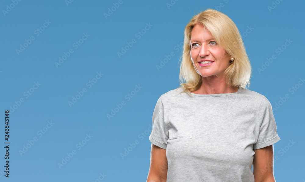 Middle age blonde woman over isolated background looking away to side with smile on face, natural expression. Laughing confident.