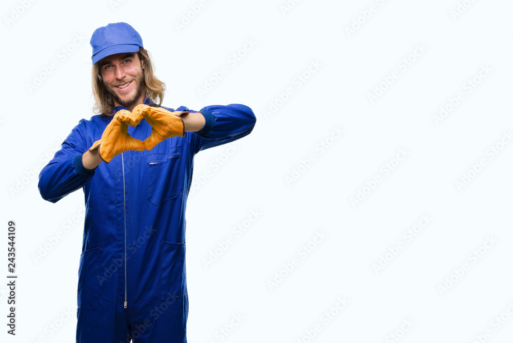 Young handsome mechanic man with long hair over isolated background smiling in love showing heart symbol and shape with hands. Romantic concept.