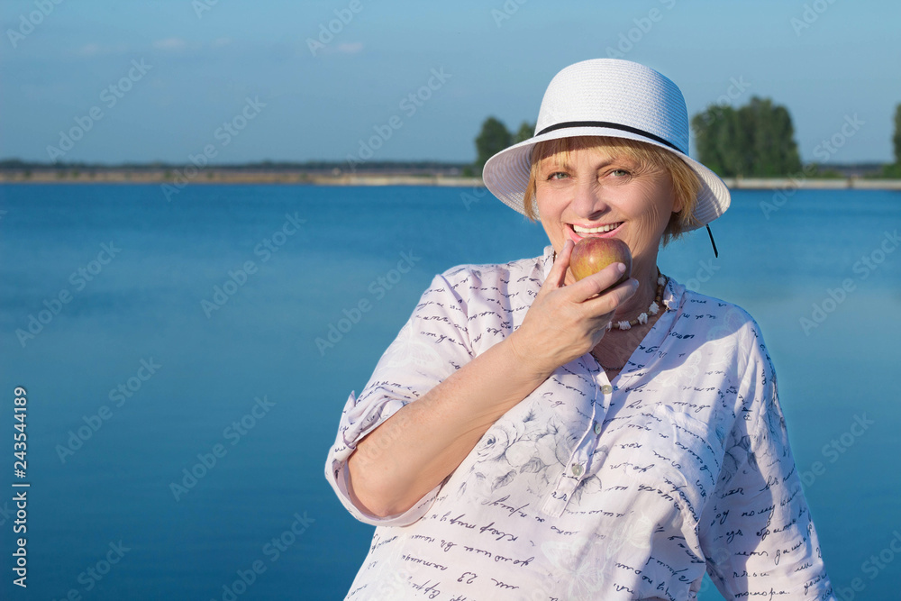Happy retired elderly lady woman bites apple showing white teeth