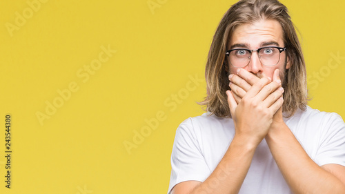 Young handsome man with long hair wearing glasses over isolated background shocked covering mouth with hands for mistake. Secret concept.
