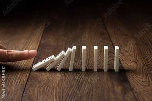 фотографія Creative background, Male hand pushing white dominoes, on a brown wooden background