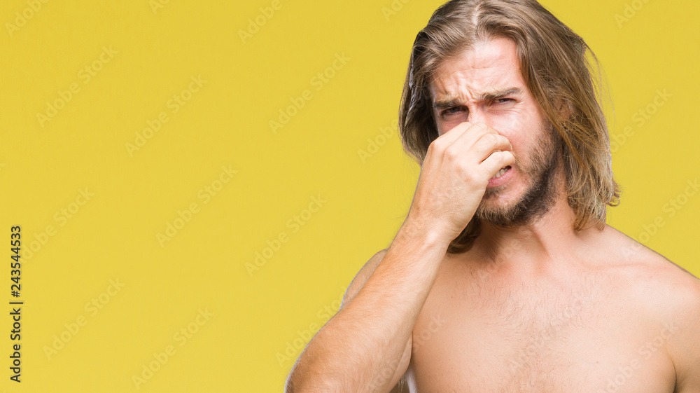 Obraz premium Young handsome shirtless man with long hair showing sexy body over isolated background smelling something stinky and disgusting, intolerable smell, holding breath with fingers on nose