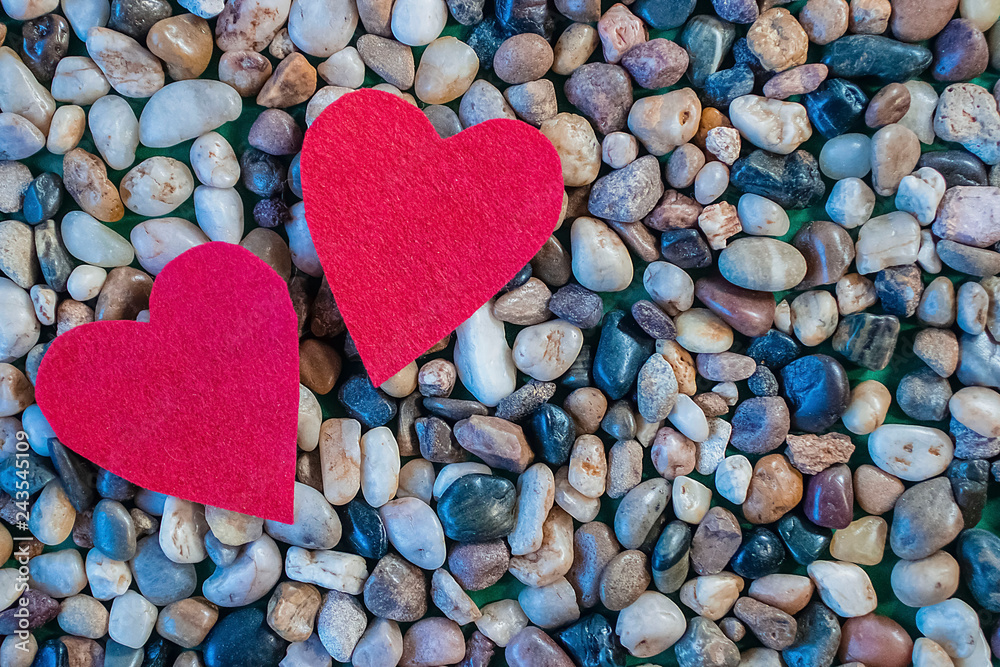 Obraz premium Two red decorative hearts and gray sea pebbles.