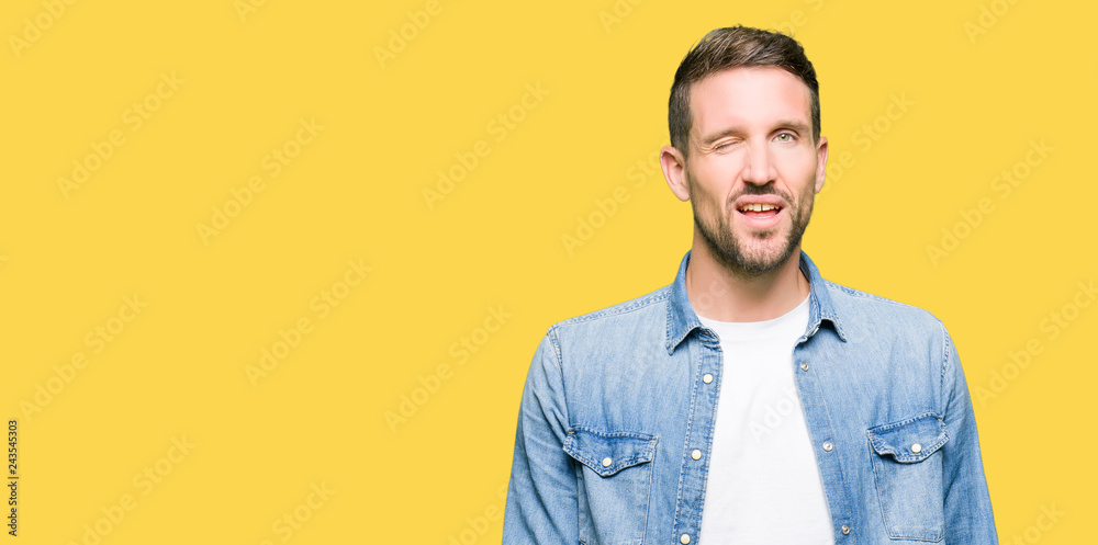 Handsome man with blue eyes and beard wearing denim jacket winking looking at the camera with sexy expression, cheerful and happy face. Handsome man with blue eyes and beard wearing denim jacket winking looking at the camera with sexy expression, cheerful and happy face.