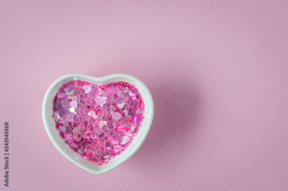Fototapeta premium Sparkles in heart shaped bowl, ceramic cup on pink background. Concept about love and relationship. Valentines Day background with hearts. Copy space, flat lay.