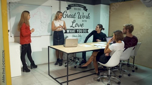 Two young women show details on whiteboard and propose new startup ideas causing a strong reaction from colleagues photo