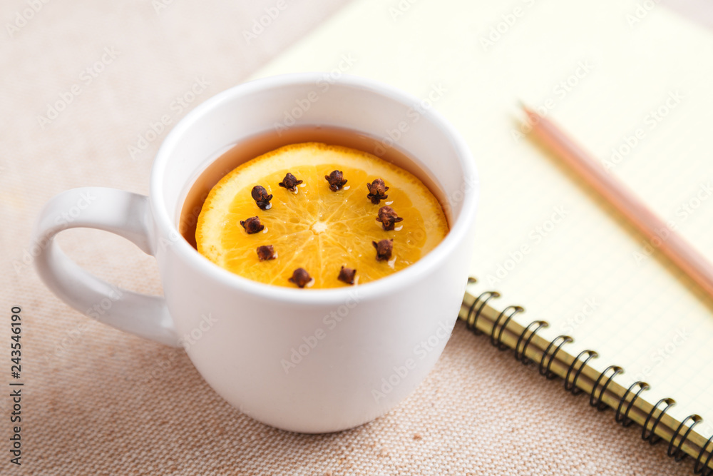 A Cup of tea with a piece of orange and cloves next to a pencil and a notebook on a table covered with a linen tablecloth, write down the list of actions. Concept of planning. Top view, copy space