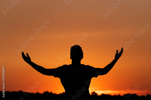 Silhouette of man clamoring to the heavens, sunset background.