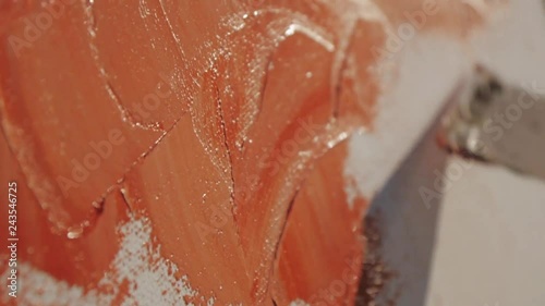 Extreme close-up shot of male artist's hand painting white canvas with a wide spatula at pebble sunrise sea beach.