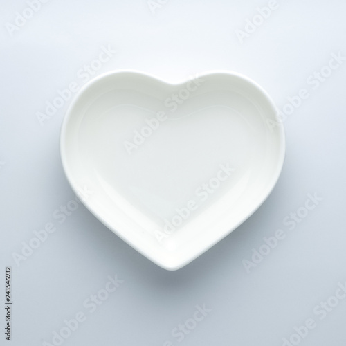 Minimalism. Empty plate in the shape of a heart on a white background in the center of the frame. Modern ceramic glossy dishes. Concept of Valentine's Day or wedding romantic theme. Square. Copyspace.