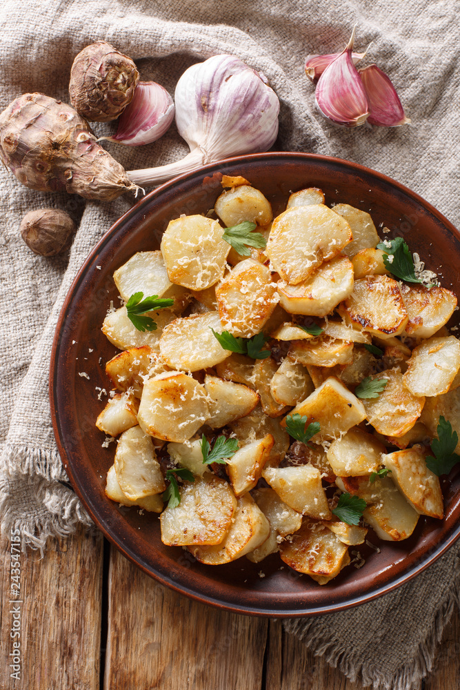 Spicy fried Jerusalem artichoke with garlic, cheese and parsley closeup on a plate. Vertical top view Spicy fried Jerusalem artichoke with garlic, cheese and parsley closeup on a plate. Vertical top view