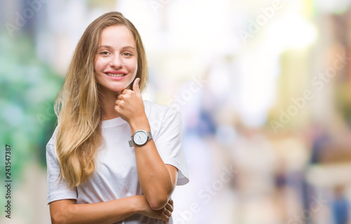 Fototapeta Naklejka Na Ścianę i Meble -  Young beautiful blonde woman wearing casual white t-shirt over isolated background looking confident at the camera with smile with crossed arms and hand raised on chin. Thinking positive.
