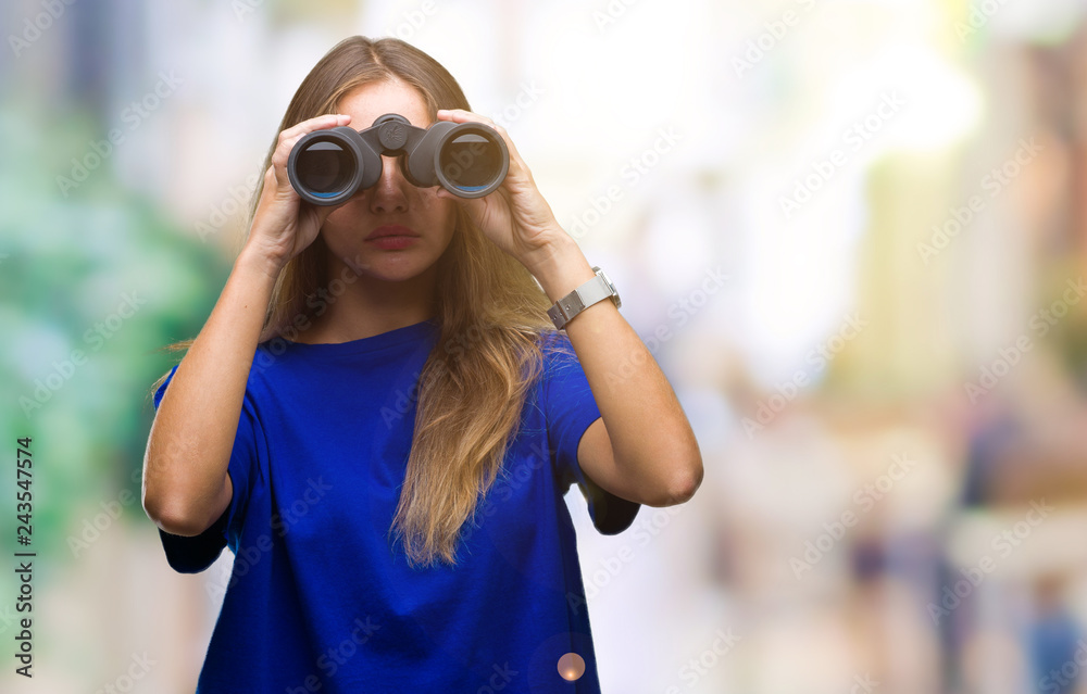 Young beautiful blonde woman looking through binoculars over isolated background with a confident expression on smart face thinking serious