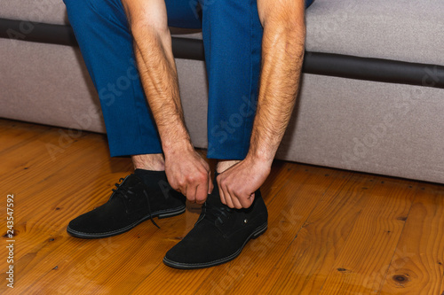 a future husband tightens up for a wedding by putting on his shoes and tying his ties.