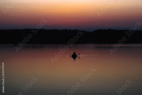 Silhouette of a man which floating on a boat on the sea at sunset time. © volhavasilevich