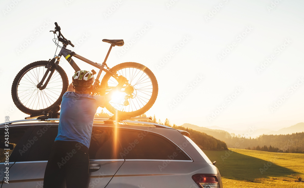 Naklejka premium Man cyclist veared in cycling clothes and protective helmet instals his mountain bike on the car roof