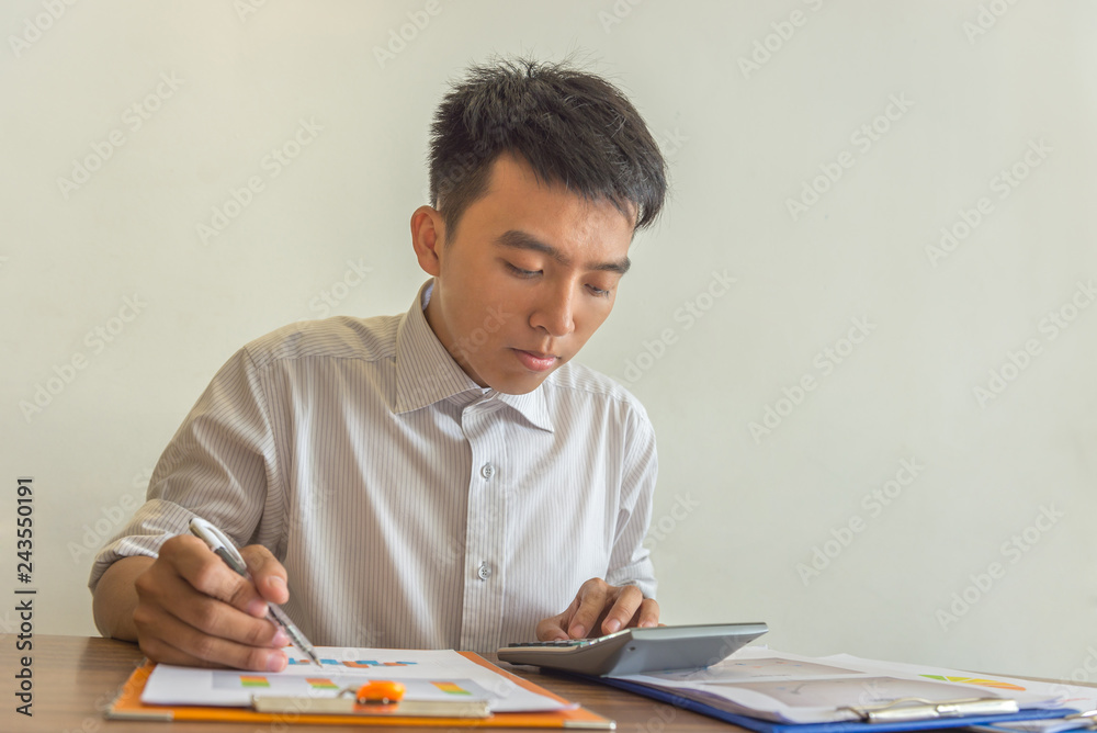 Young man using calculator and reading financial reports Young man using calculator and reading financial reports