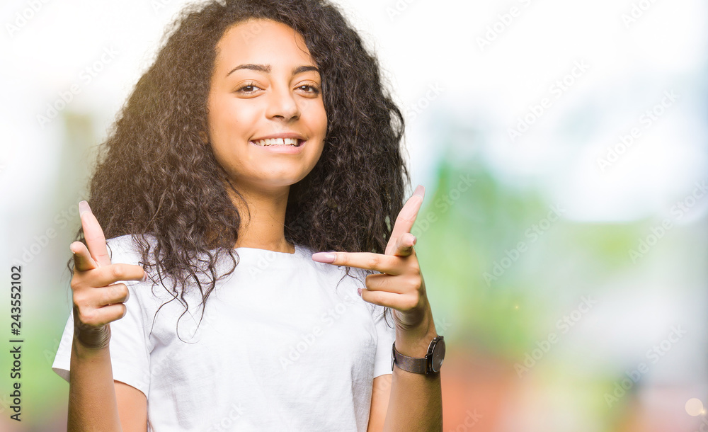 Young beautiful girl with curly hair wearing casual white t-shirt pointing fingers to camera with happy and funny face. Good energy and vibes. Young beautiful girl with curly hair wearing casual white t-shirt pointing fingers to camera with happy and funny face. Good energy and vibes.