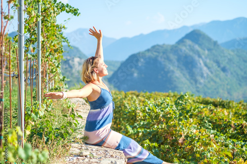 Young pretty blonde woman enjoys outdoor recreation and admires the picturesque landscape. Mountains covered with green forest is seen in a background. Bright sunny day