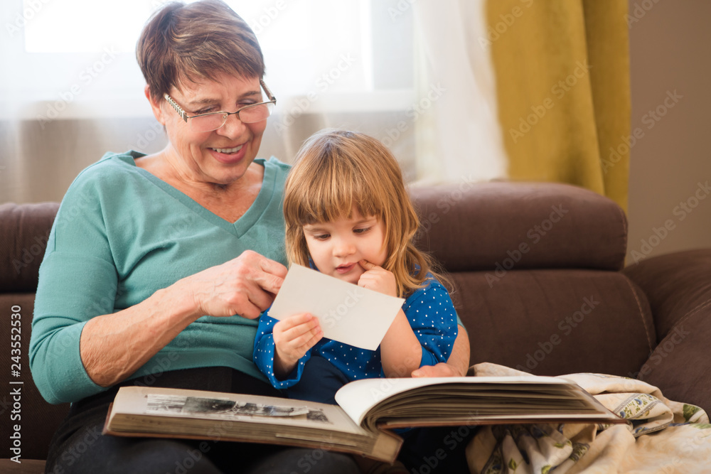 Grandmother with child granddaughter having a great time and looking old family photo album at home.
Grandmother with child granddaughter having a great time and looking old family photo album at home.
