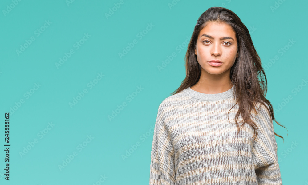 Young beautiful arab woman wearing winter sweater over isolated background with serious expression on face. Simple and natural looking at the camera. Young beautiful arab woman wearing winter sweater over isolated background with serious expression on face. Simple and natural looking at the camera.