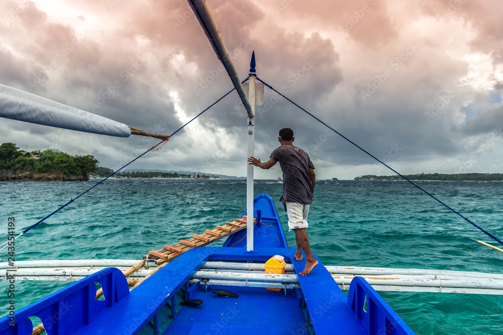 Young filipino man standing at edge of yacht looking at sea. Travelling on old boat at cloudy day.