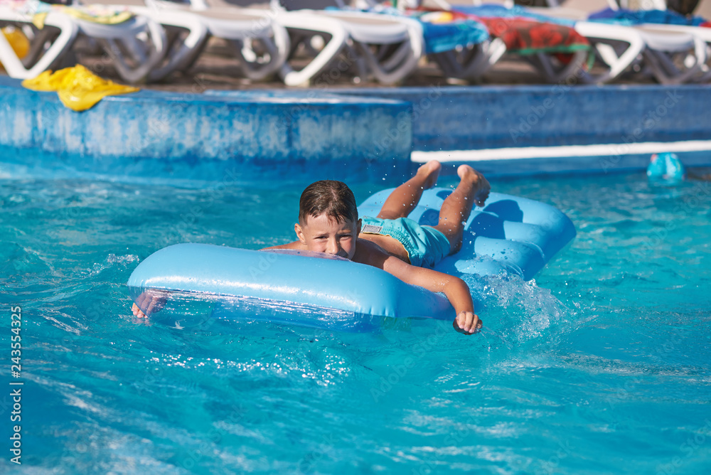 Smiling European boy is swimming on the inflatable blue floater in the hotel’s pool. He is having fun during his summer vacations.