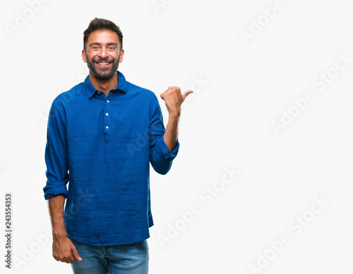 Adult hispanic man over isolated background smiling with happy face looking and pointing to the side with thumb up.