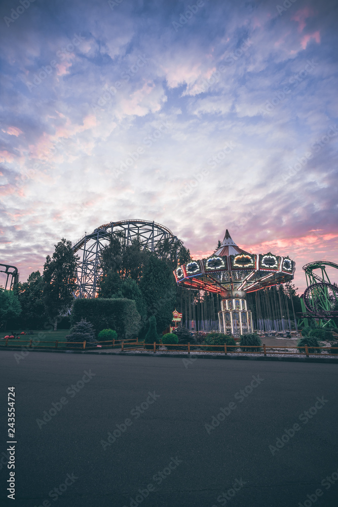 Fototapeta premium Amusement Park with carousel and Rollercoaster, night lights, sunset