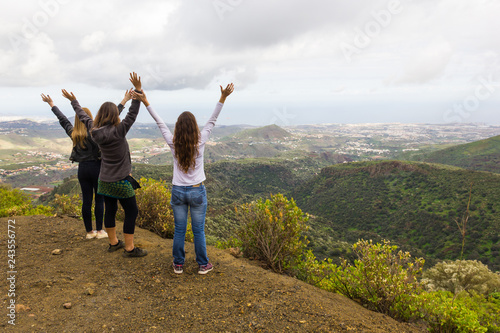 Three women with arms up celebrating great views from mountain top on cloudy day in Gran Canaria island. Girl friends hiking in Canary Islands. Outdoors leisure activity, nature connection concepts
