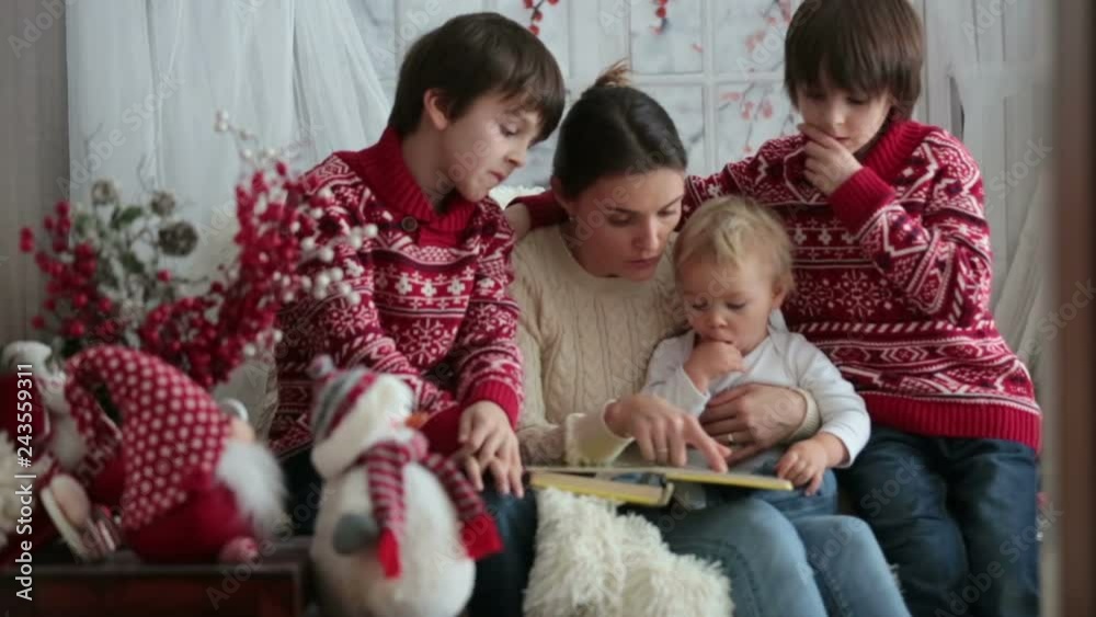 Mother reads book to her sons, children sitting in cozy armchair on a snowy winter day, wintertime Mother reads book to her sons, children sitting in cozy armchair on a snowy winter day, wintertime