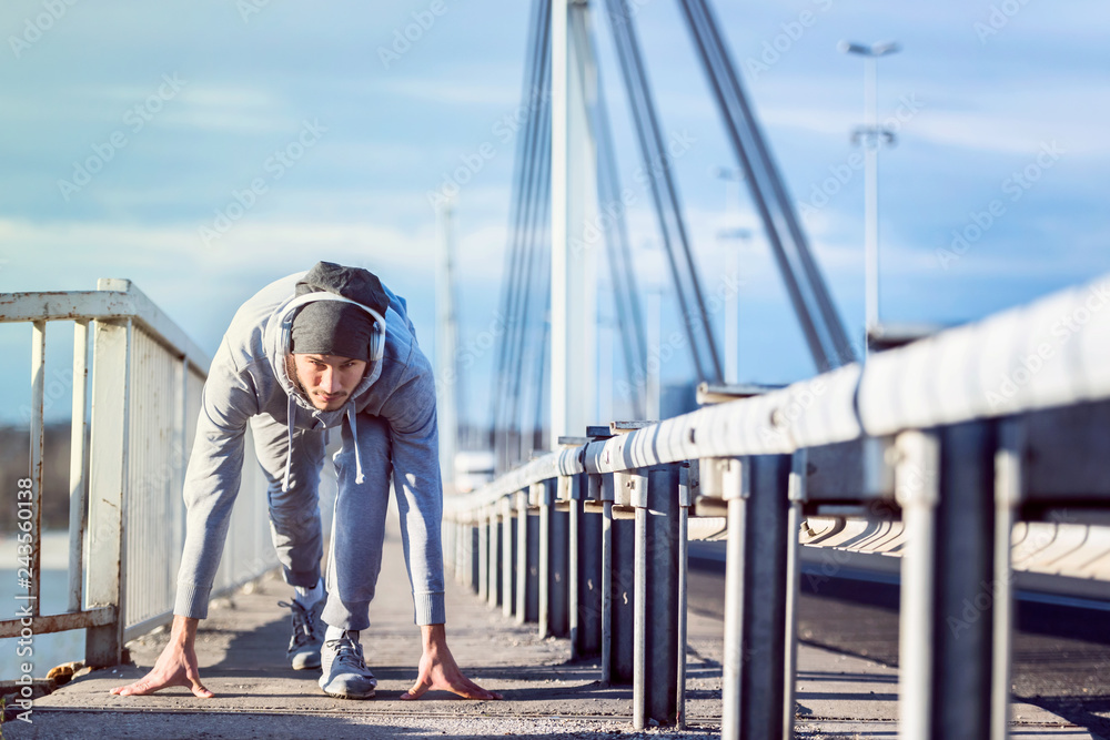 Young sports man with earphones running on the bridge outside in a city. Extreme running challenge