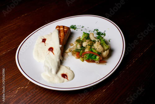 Appetizing dish on a white plate stands on a wooden table, food, snack