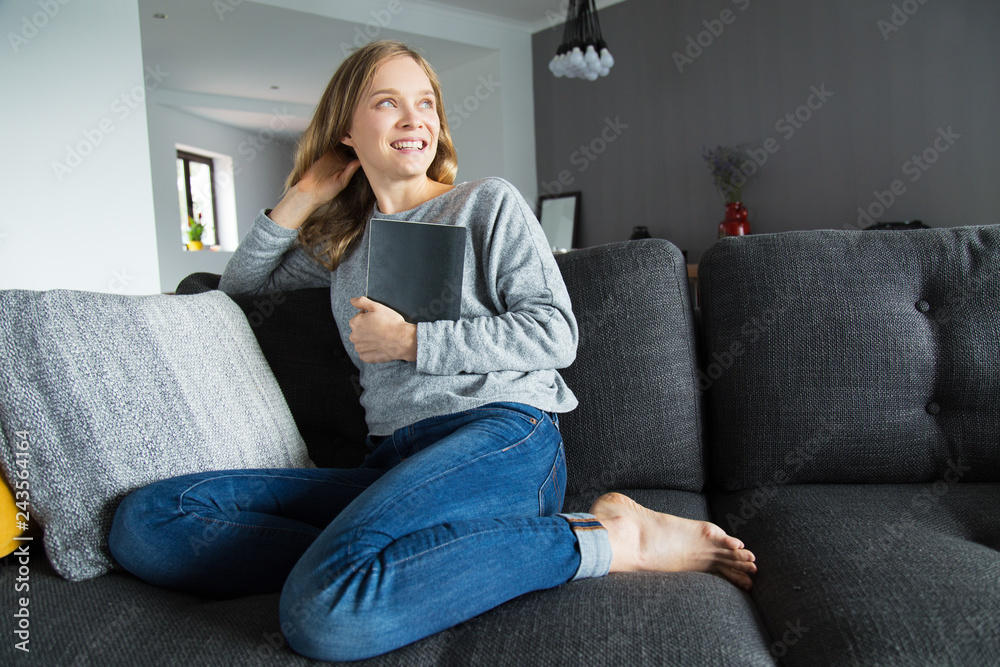 Cheerful female student done with her home assignment. Young woman in casual sitting on couch in living room and holding notebook. Happy bookworm concept Cheerful female student done with her home assignment. Young woman in casual sitting on couch in living room and holding notebook. Happy bookworm concept