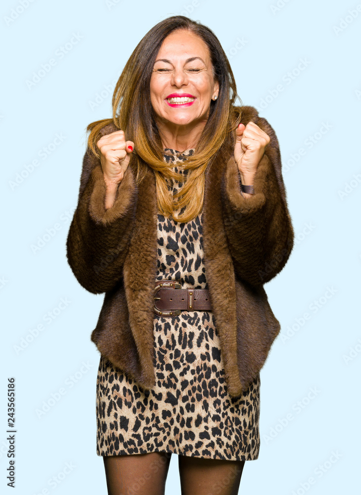 Beautiful middle age elegant woman wearing mink coat excited for success with arms raised celebrating victory smiling. Winner concept.