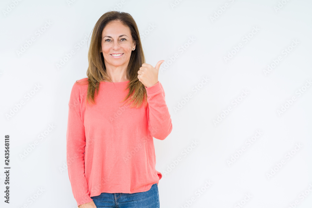 Beautiful middle age woman over isolated background smiling with happy face looking and pointing to the side with thumb up. Beautiful middle age woman over isolated background smiling with happy face looking and pointing to the side with thumb up.