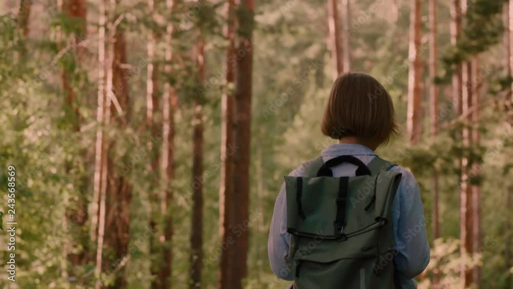 Woman hipster traveller enjoying wonderful nature and looking around low angle medium shot female backpacker having good time in summer forest back view steadicam establish shot Woman hipster traveller enjoying wonderful nature and looking around low angle medium shot female backpacker having good time in summer forest back view steadicam establish shot