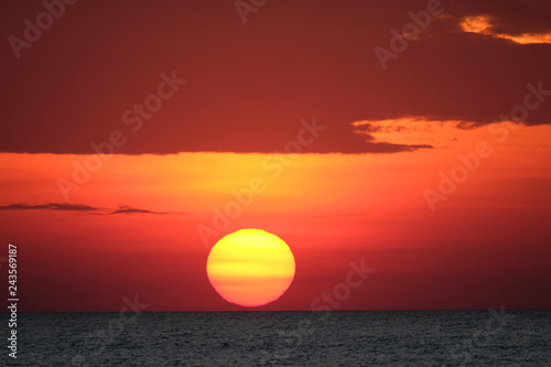 Fototapeta Naklejka Na Ścianę i Meble -  Impressive sunset over the sea  with dramatic red fiery sky and dark clouds. Huge glowing orange red  sun nearly touch the horizon.