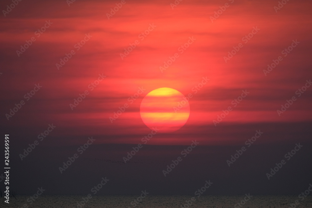 Impressive sunset over the sea with dramatic red fiery sky and dark clouds. Huge glowing orange red sun nearly touch the horizon. Amazing beautiful romantic evening at the beach and perfect vacation. Impressive sunset over the sea with dramatic red fiery sky and dark clouds. Huge glowing orange red sun nearly touch the horizon. Amazing beautiful romantic evening at the beach and perfect vacation.