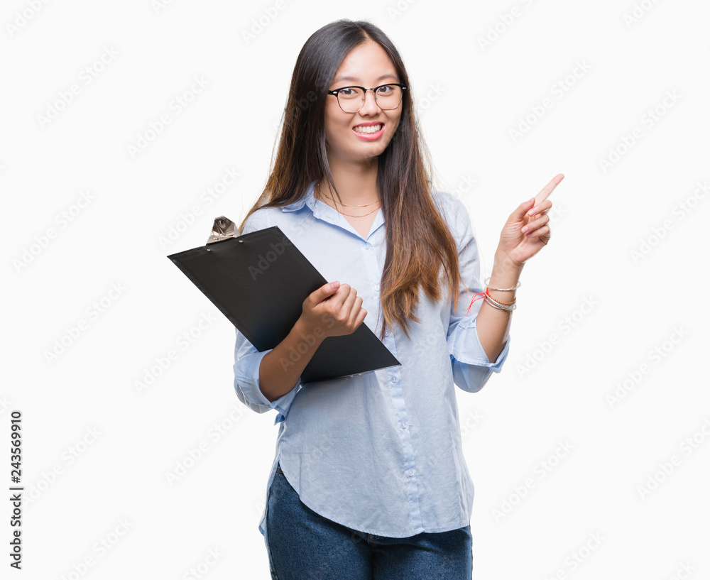 Young asian business woman holding clipboard over isolated background very happy pointing with hand and finger to the side Young asian business woman holding clipboard over isolated background very happy pointing with hand and finger to the side