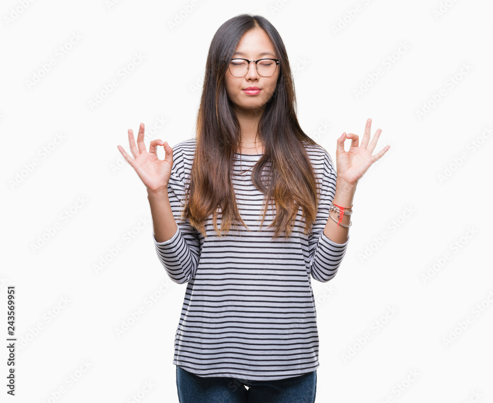 Young asian woman wearing glasses over isolated background relax and smiling with eyes closed doing meditation gesture with fingers. Yoga concept. Young asian woman wearing glasses over isolated background relax and smiling with eyes closed doing meditation gesture with fingers. Yoga concept.