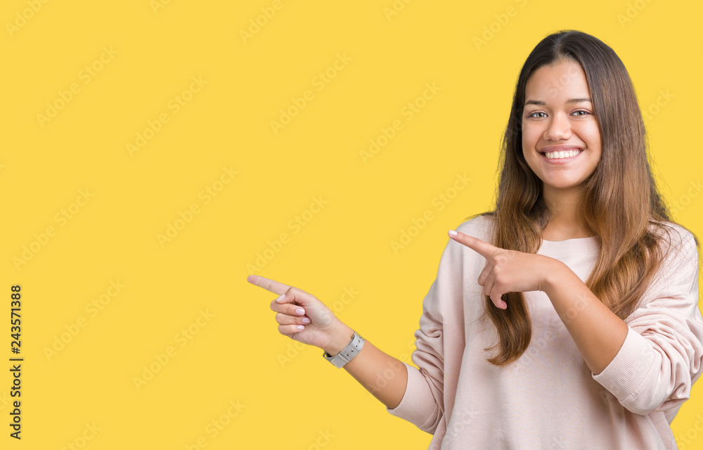 Young beautiful brunette woman wearing pink sweatshirt over isolated background smiling and looking at the camera pointing with two hands and fingers to the side. Young beautiful brunette woman wearing pink sweatshirt over isolated background smiling and looking at the camera pointing with two hands and fingers to the side.