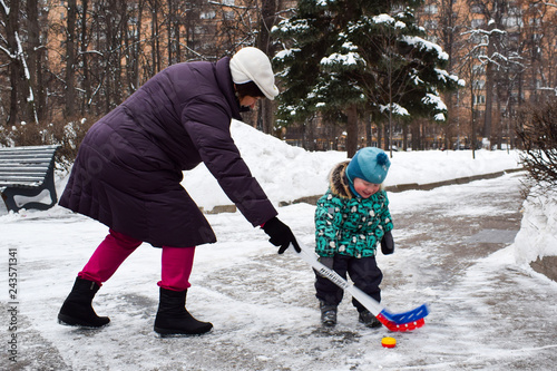 Grandmother and little two-year-old grandson have fun playing hockey in the park in winter