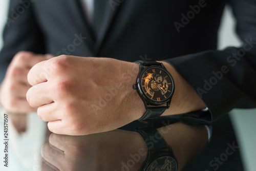 Closeup of businessman wrist wearing watch. Business leader sitting at glossy table during meeting. Business accessory concept