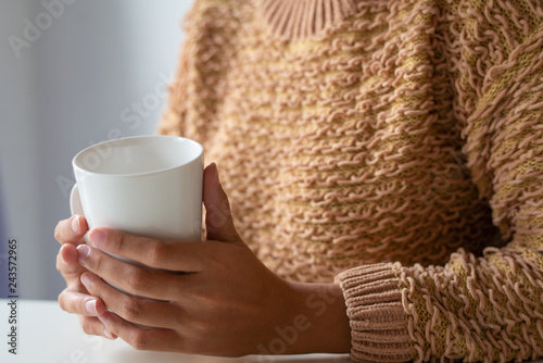 Close-up of lady in fluffy sweater drinking from mug. Unrecognizable woman having coffee break. Winter concept