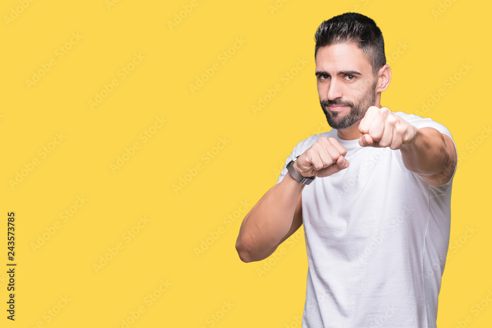 Handsome man wearing white t-shirt over yellow isolated background Punching fist to fight 