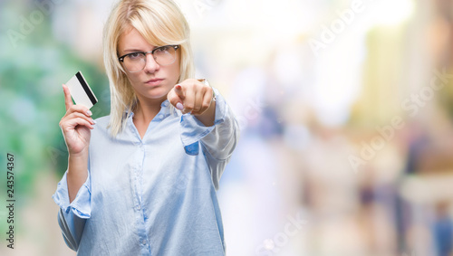 Young beautiful blonde business woman holding credit card over isolated background pointing with finger to the camera and to you  hand sign  positive and confident gesture from the front