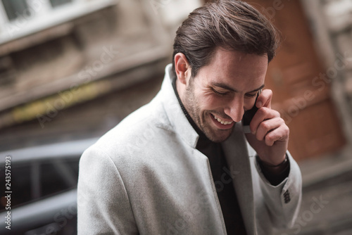 Handsome young fashionable man enjoying a happy conversation on his phone, walking the street of a city