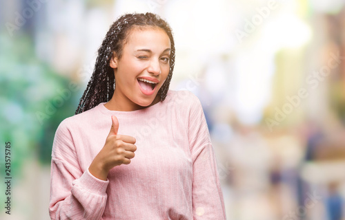 Young braided hair african american girl wearing sweater over isolated background winking looking at the camera with sexy expression, cheerful and happy face.